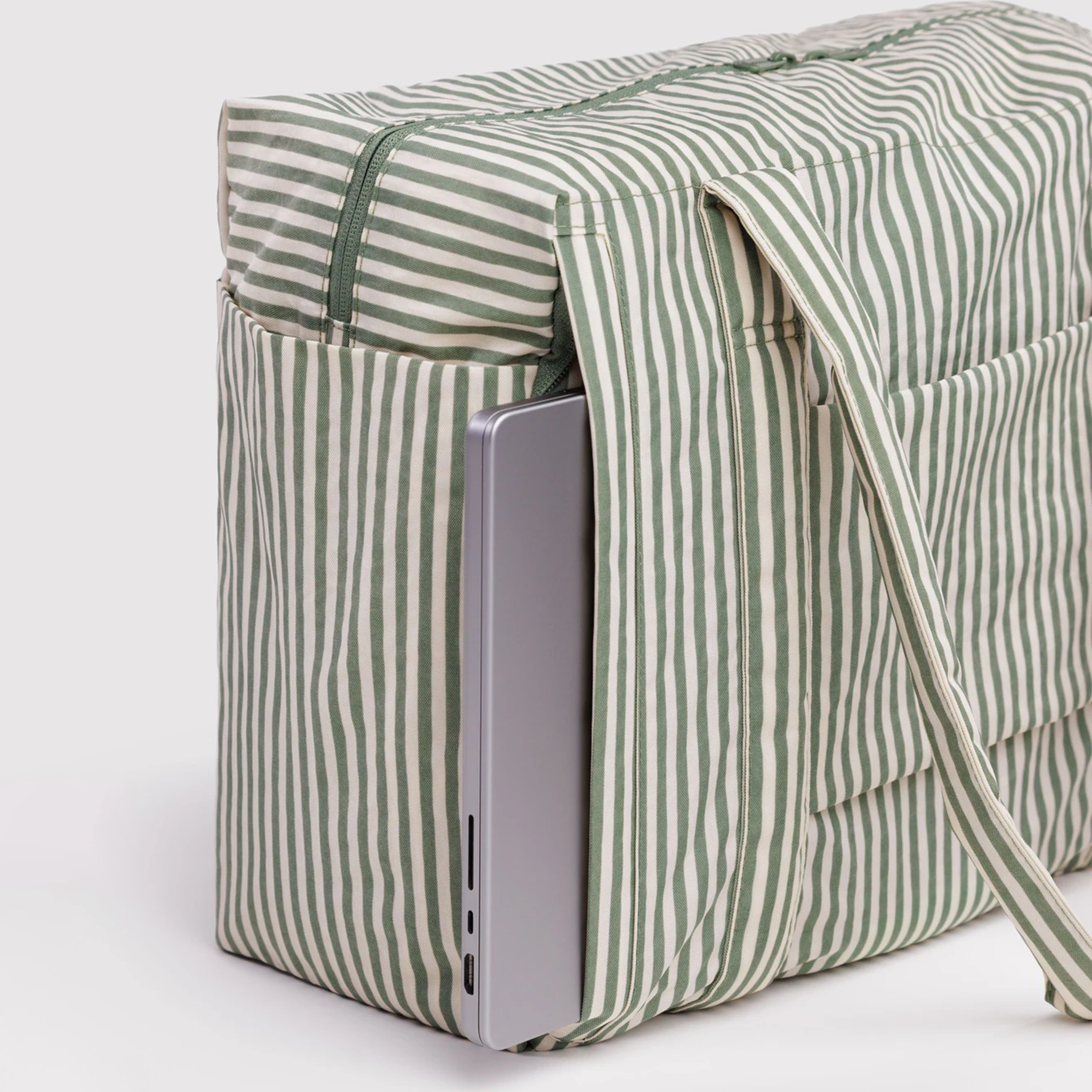 A sage striped nylon carry on bag with a silver laptop peeking out the side.