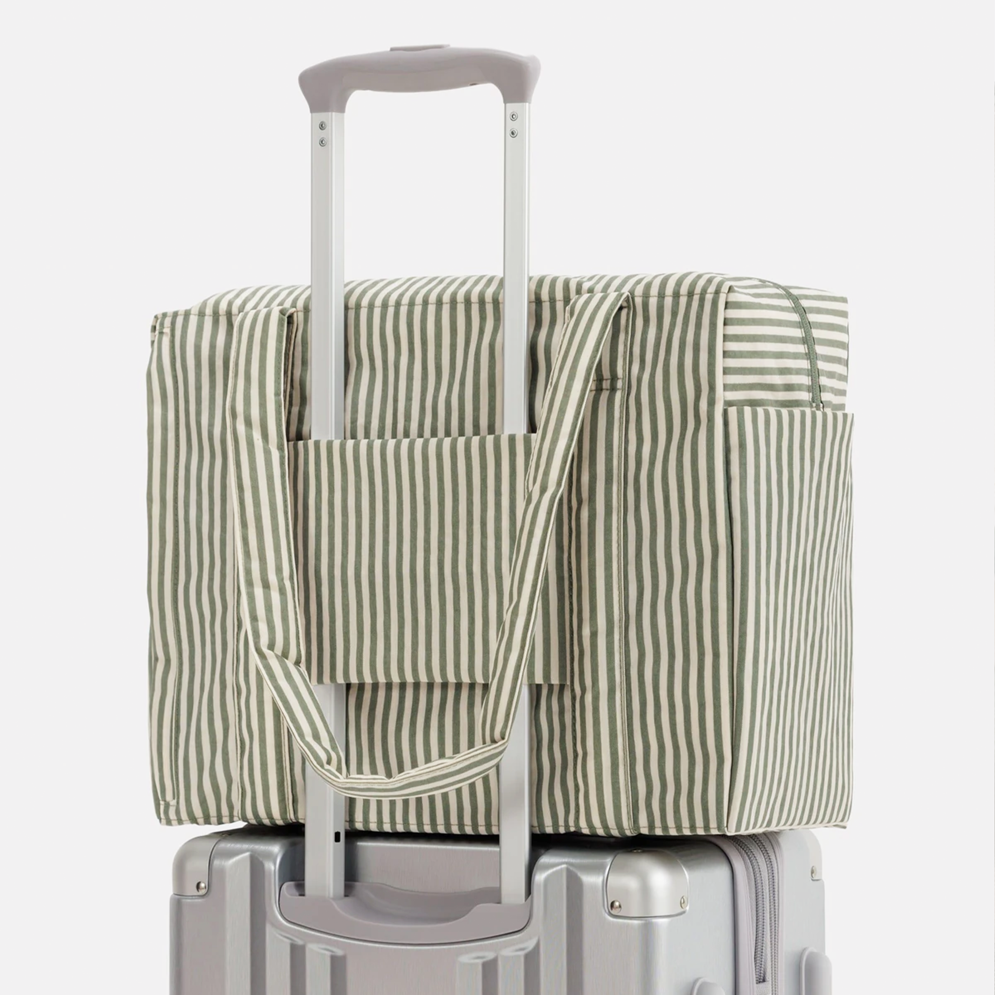 A sage striped nylon carry on bag on top of a silver suitcase.