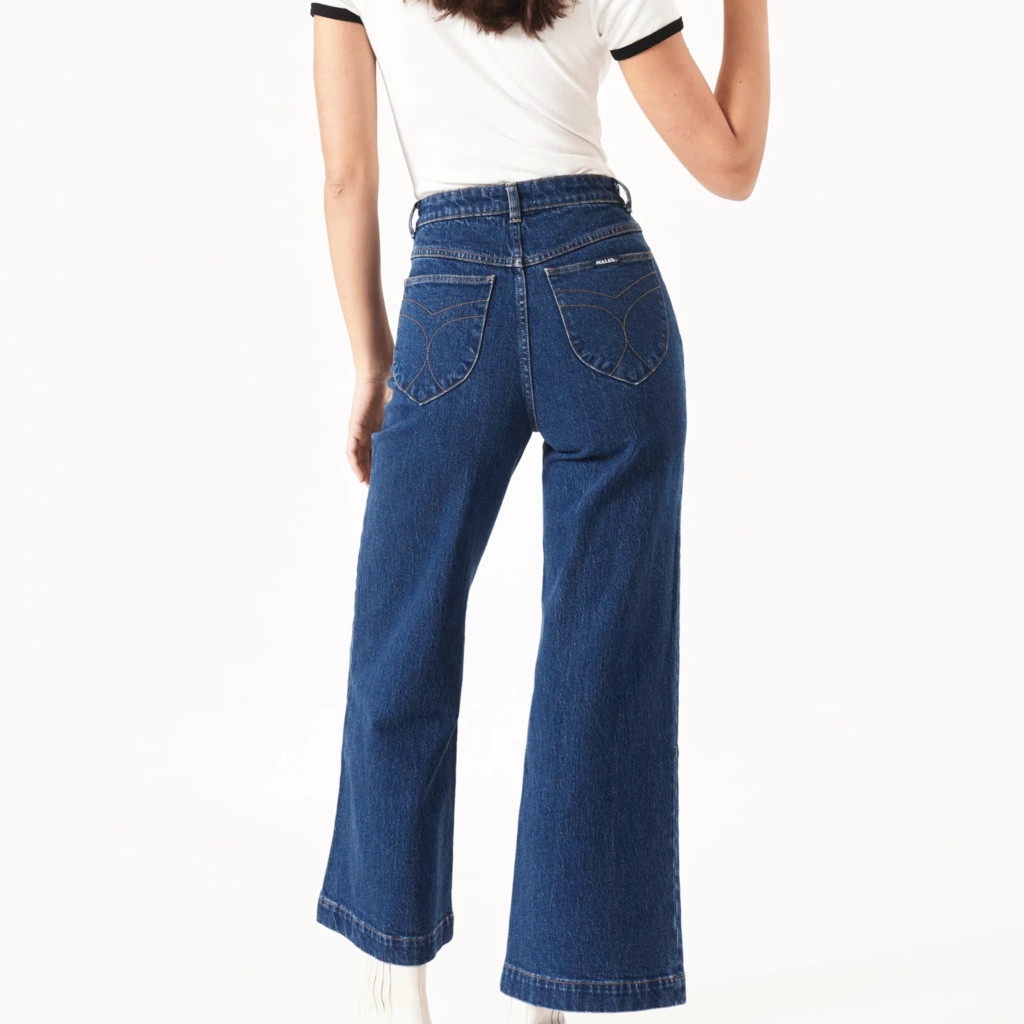 On a white background is a model wearing a dark blue pair of denim jeans with front pockets, a high waist and flair bottoms.