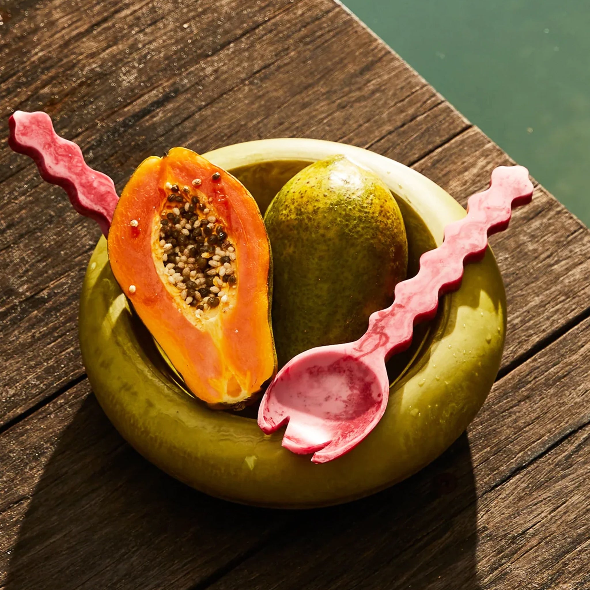 Papaya and lime in a green bowl with pink spoons on a wooden surface