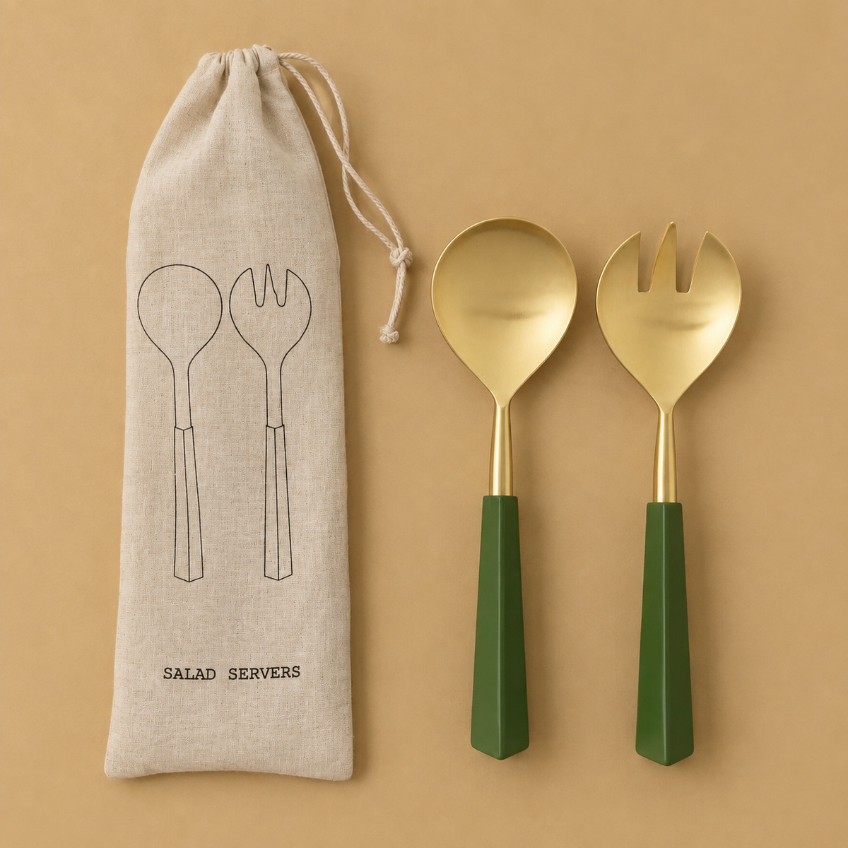 A set of salad servers with gold-toned heads and dark green handles, displayed next to a beige drawstring pouch printed with the words 'SALAD SERVERS' and simple line drawings of the utensils, all on a warm tan background.