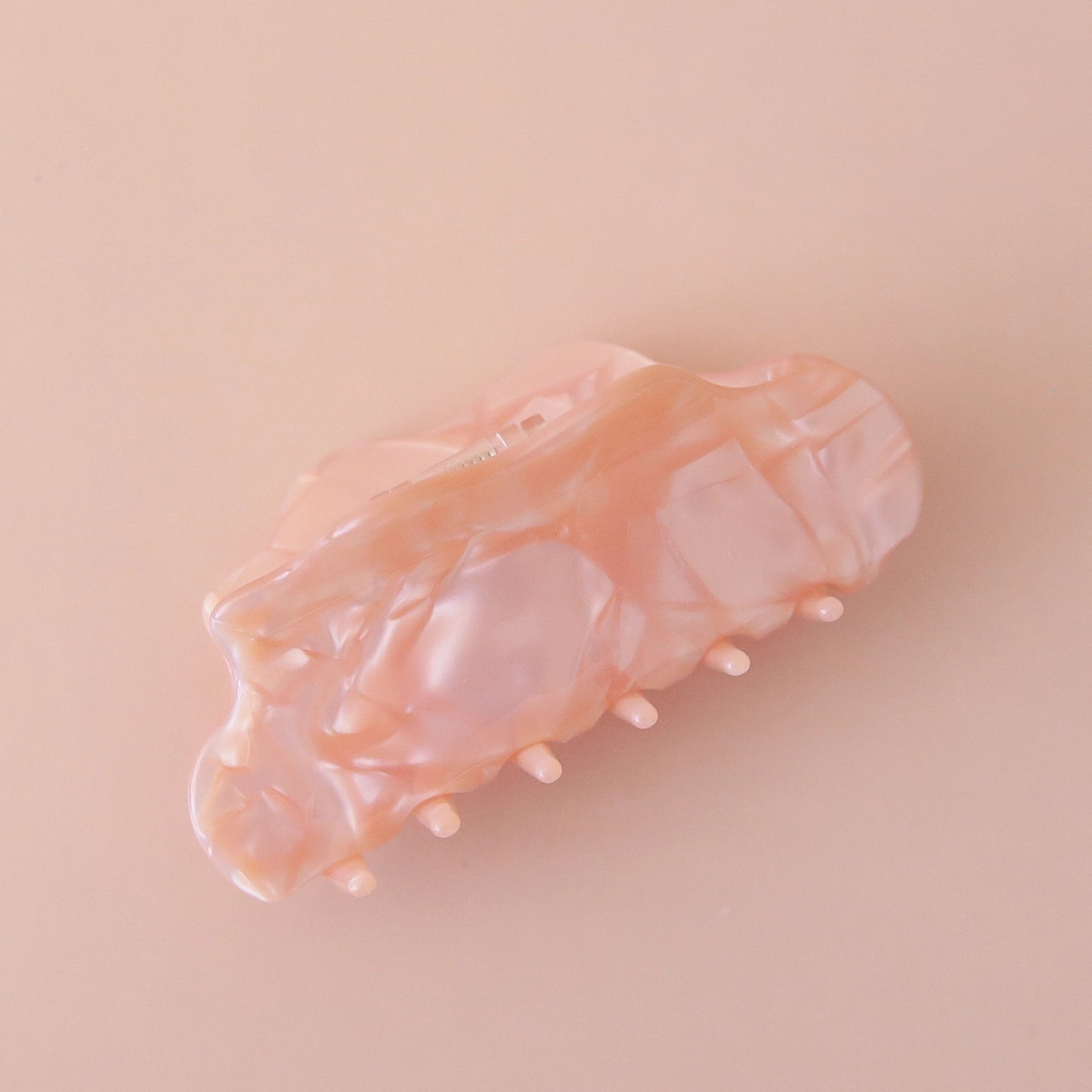 On a pink background is a light pink hair clip with a shell texture. 
