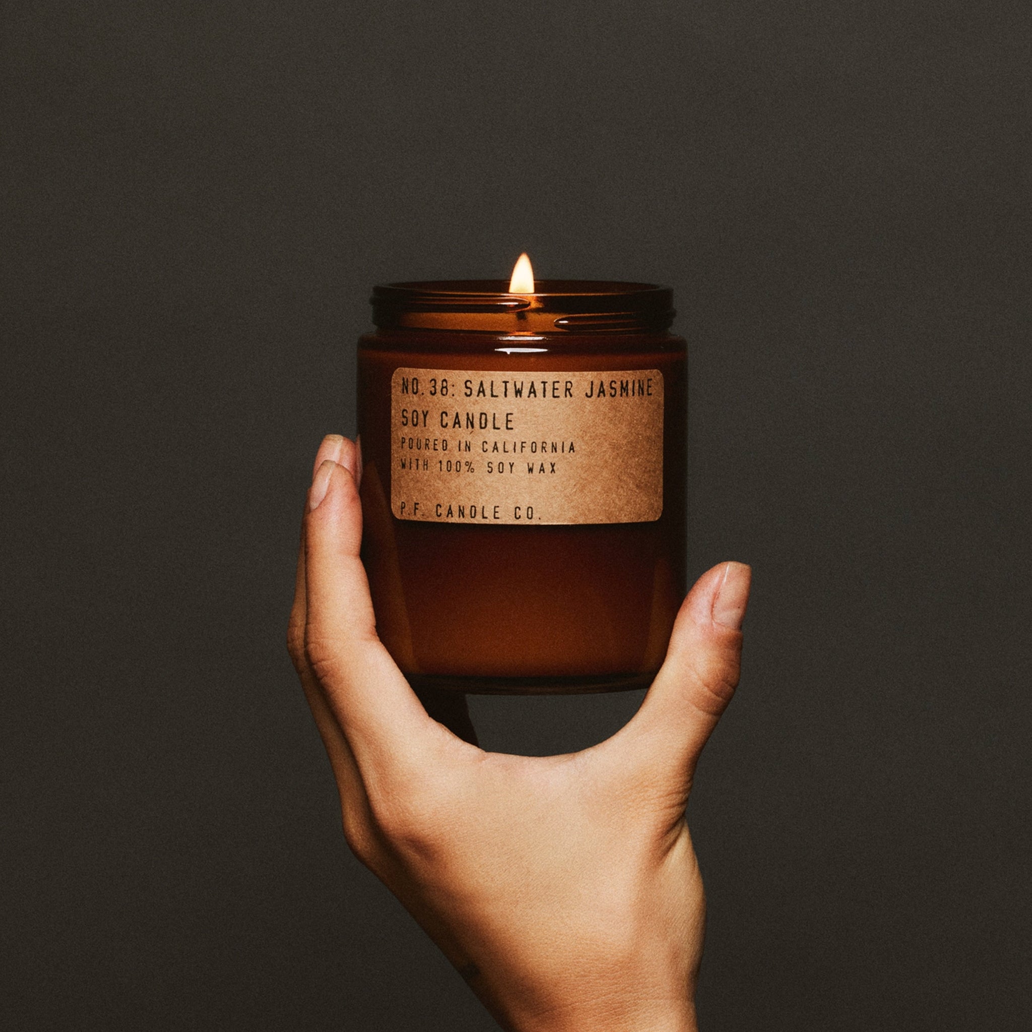 Hand holding a lit candle with a label against a dark background