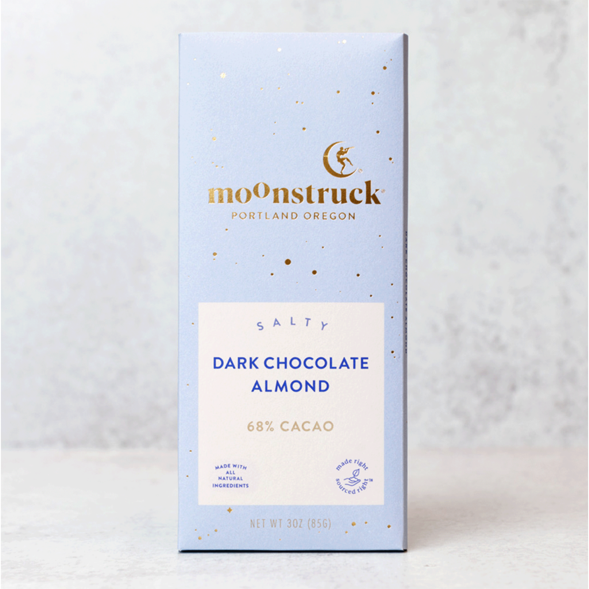 On a grey background is a light blue packaged chocolate bar with gold details and text that reads, "moonstruck Portland Oregon", "Salty Dark Chocolate Almond 68% Cacao".