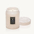 In front of a white background is a light pink glass cylinder jar. The jar has a floral pattern on it. In the middle is a black rectangular sticker with a gold border. There is gold text at the top that reads ‘voluspa.’ Below is white text that reads santal vanille.’ There is a matching lid leaning against the right side of the jar.