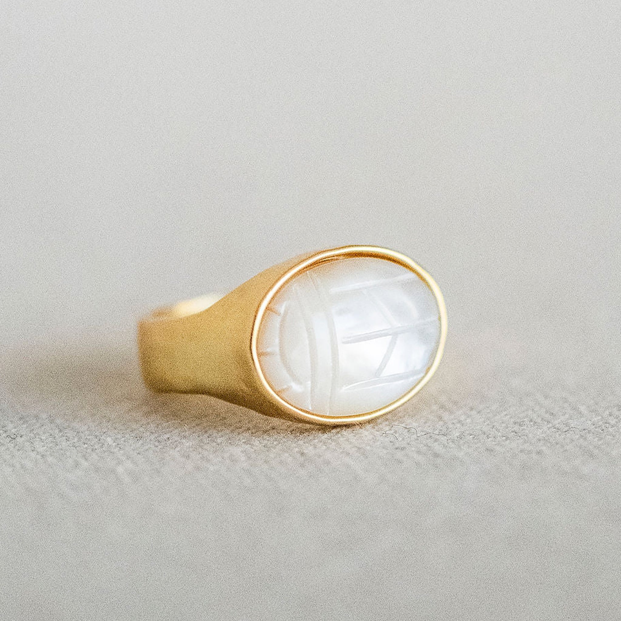 A gold oval mother of pearl stone sitting in a gold plated setting. 