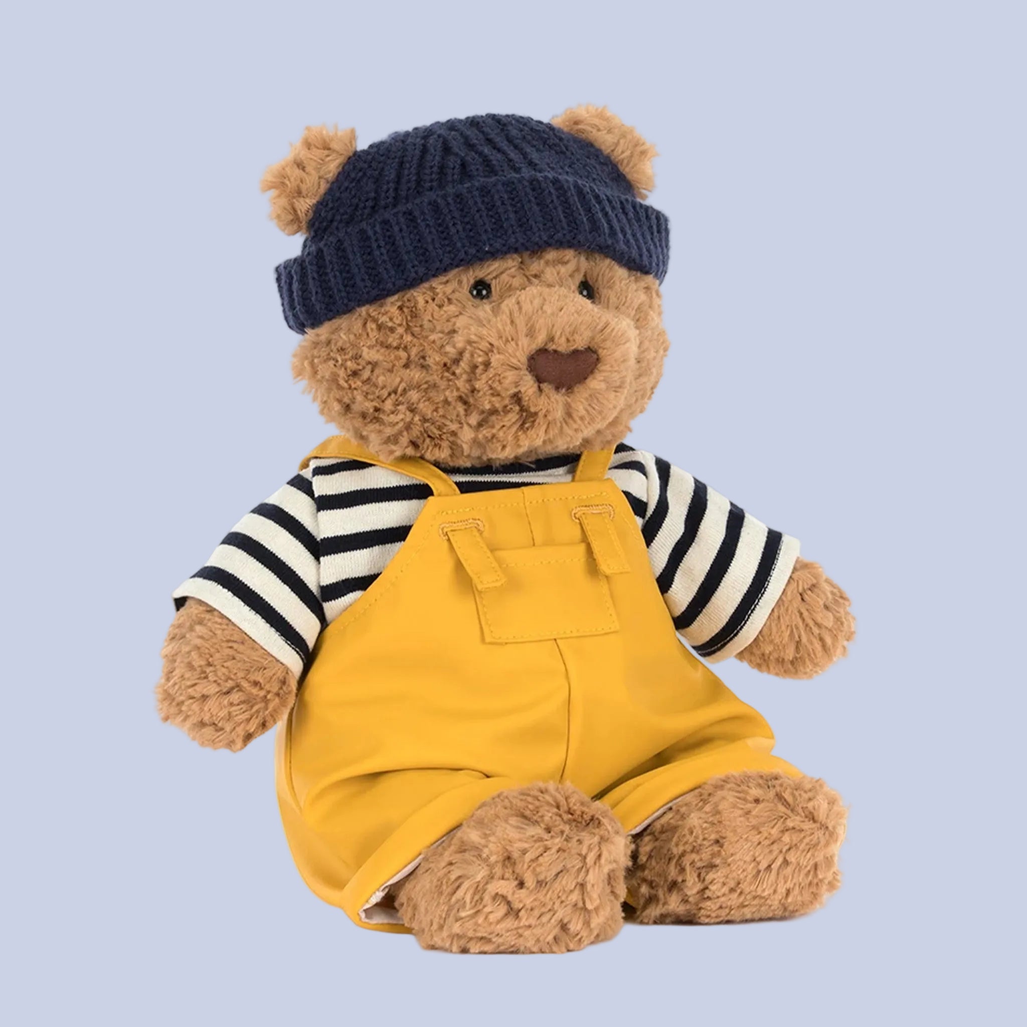 Teddy bear wearing a navy hat, striped shirt, and yellow overalls on a white background