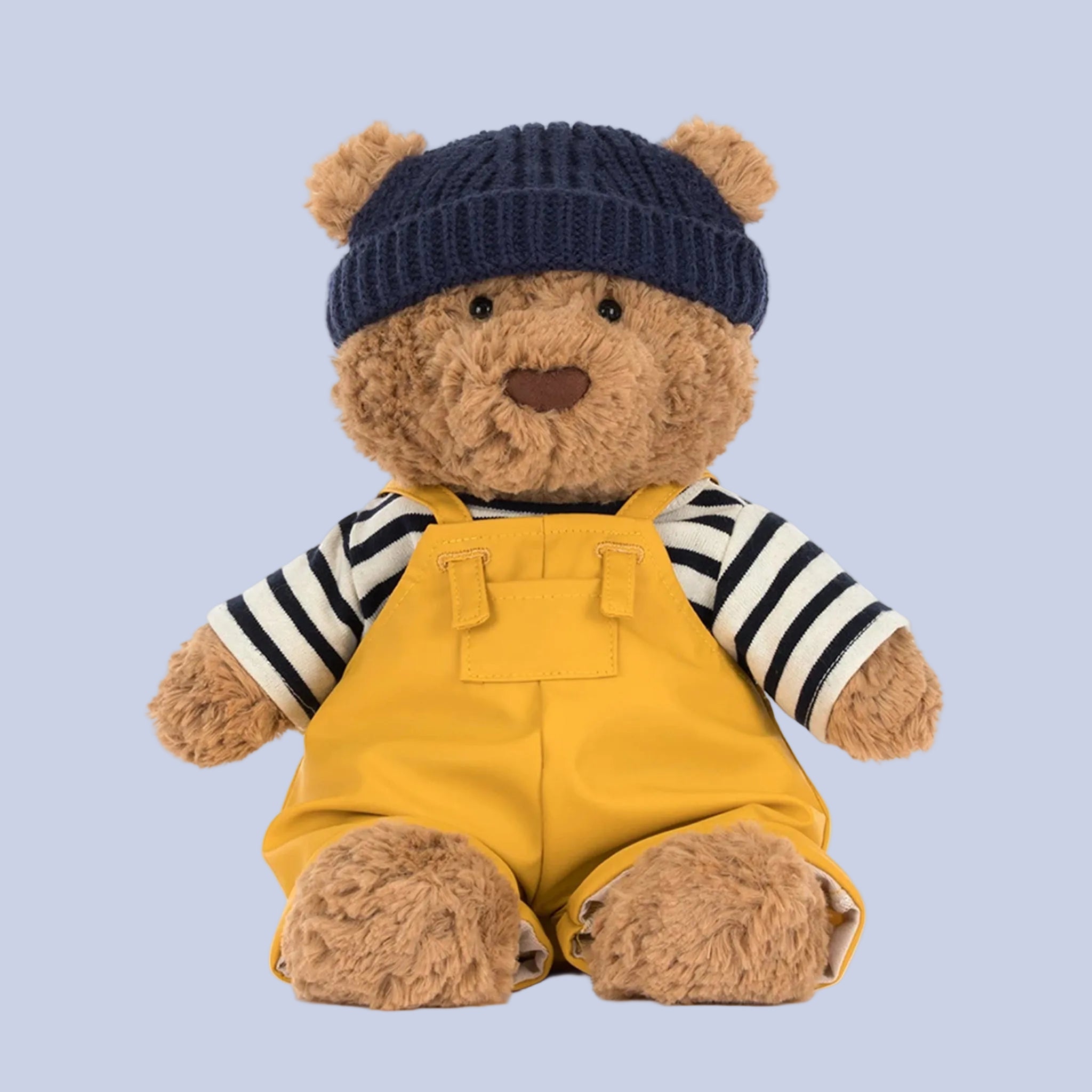 Teddy bear wearing a navy hat, striped shirt, and yellow overalls on a white background