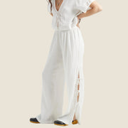 A pair of linen flowy wide leg pants with an eyelet edge and tie detail on the outside bottom edges. 