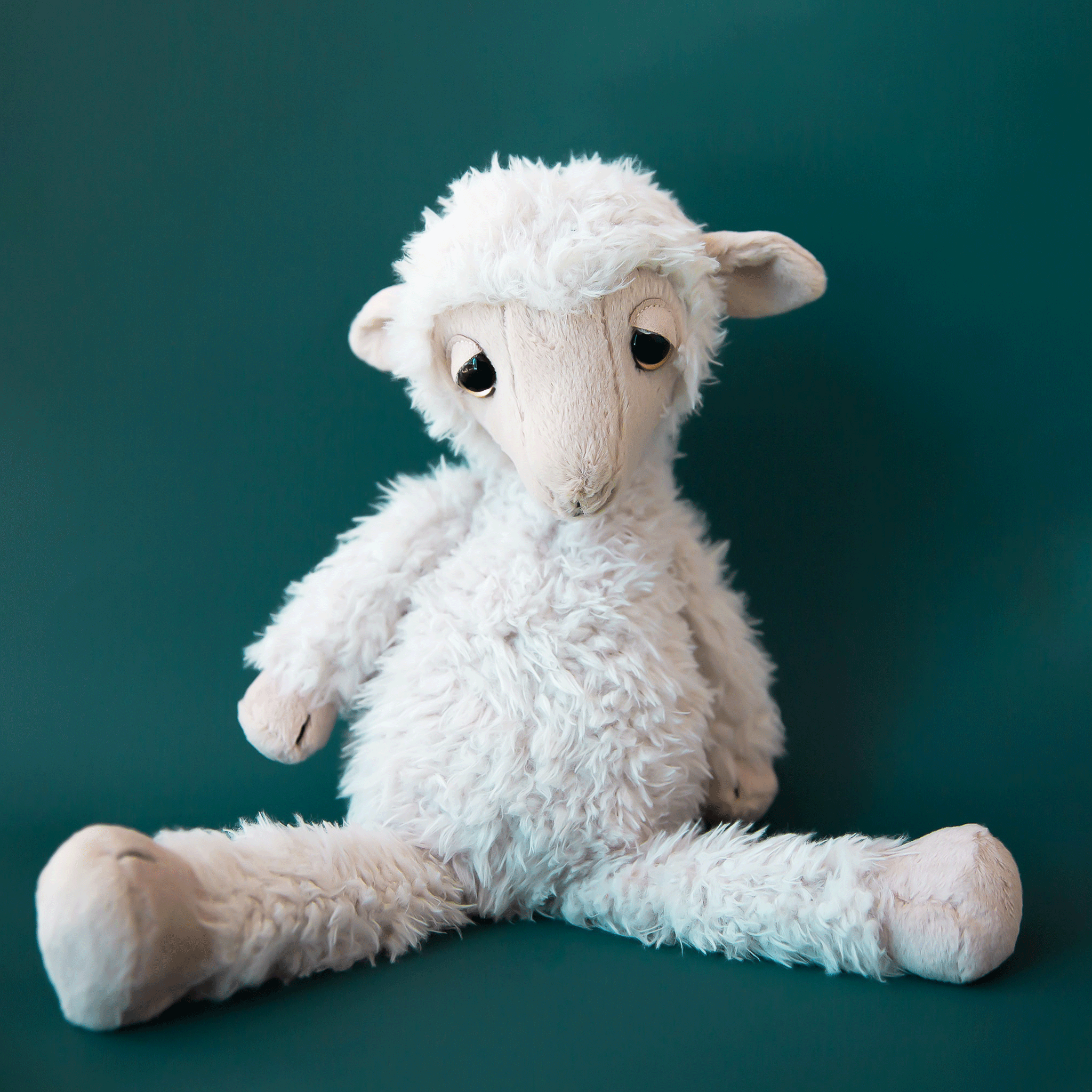 On a teal background is an ivory stuffed animal sheep with sleepy eyes.