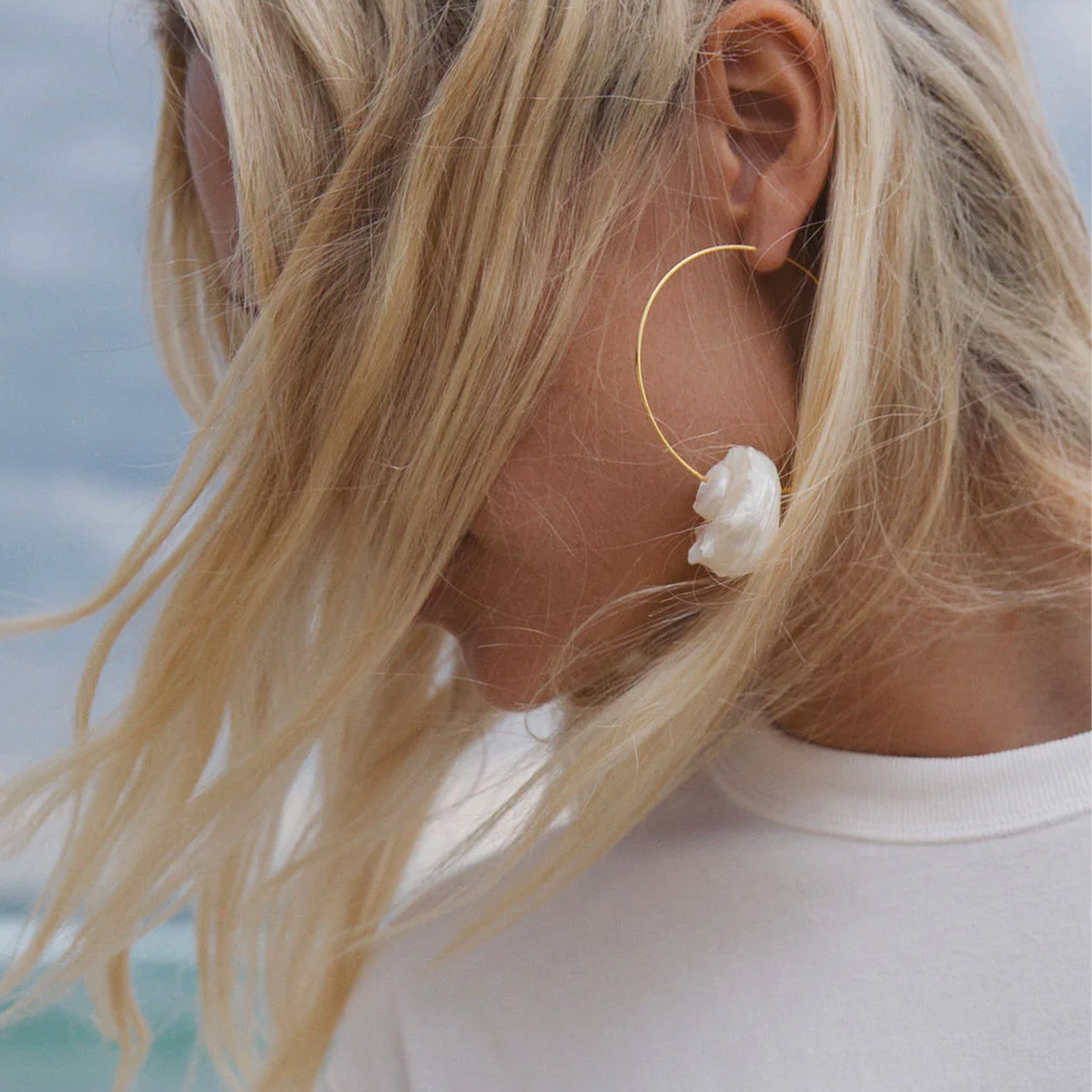 A pair of gold hoop earrings with a white shell on each hoop. 