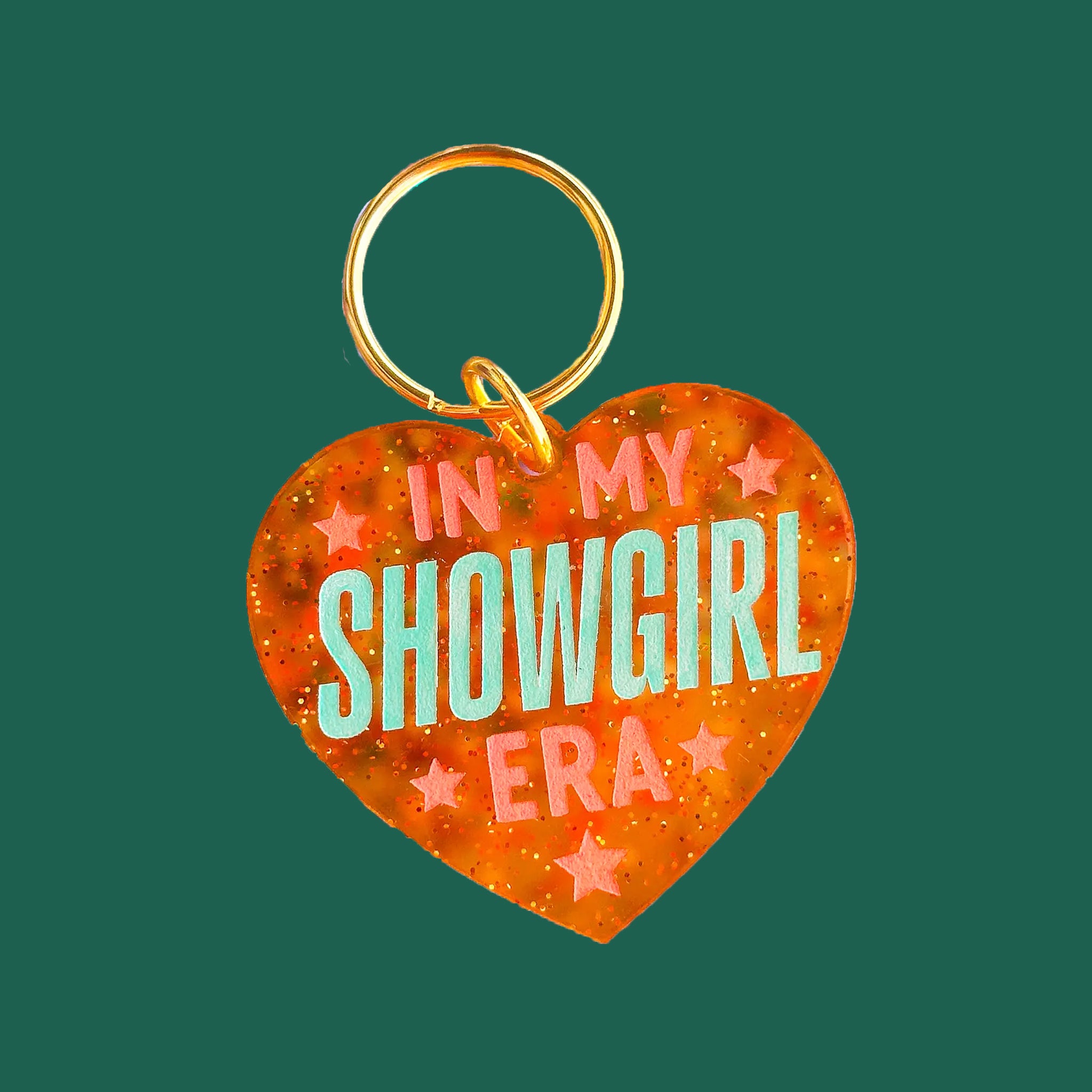 An orange heart shaped keychain with text that reads, 'In My Showgirl Era". 