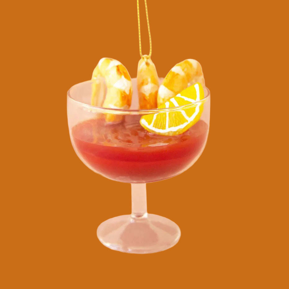 Cocktail glass with red cocktail sauce, three shrimps and a lemon wedge. 