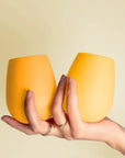A pair of stemless silicone cups, one light yellow and the other darker. 