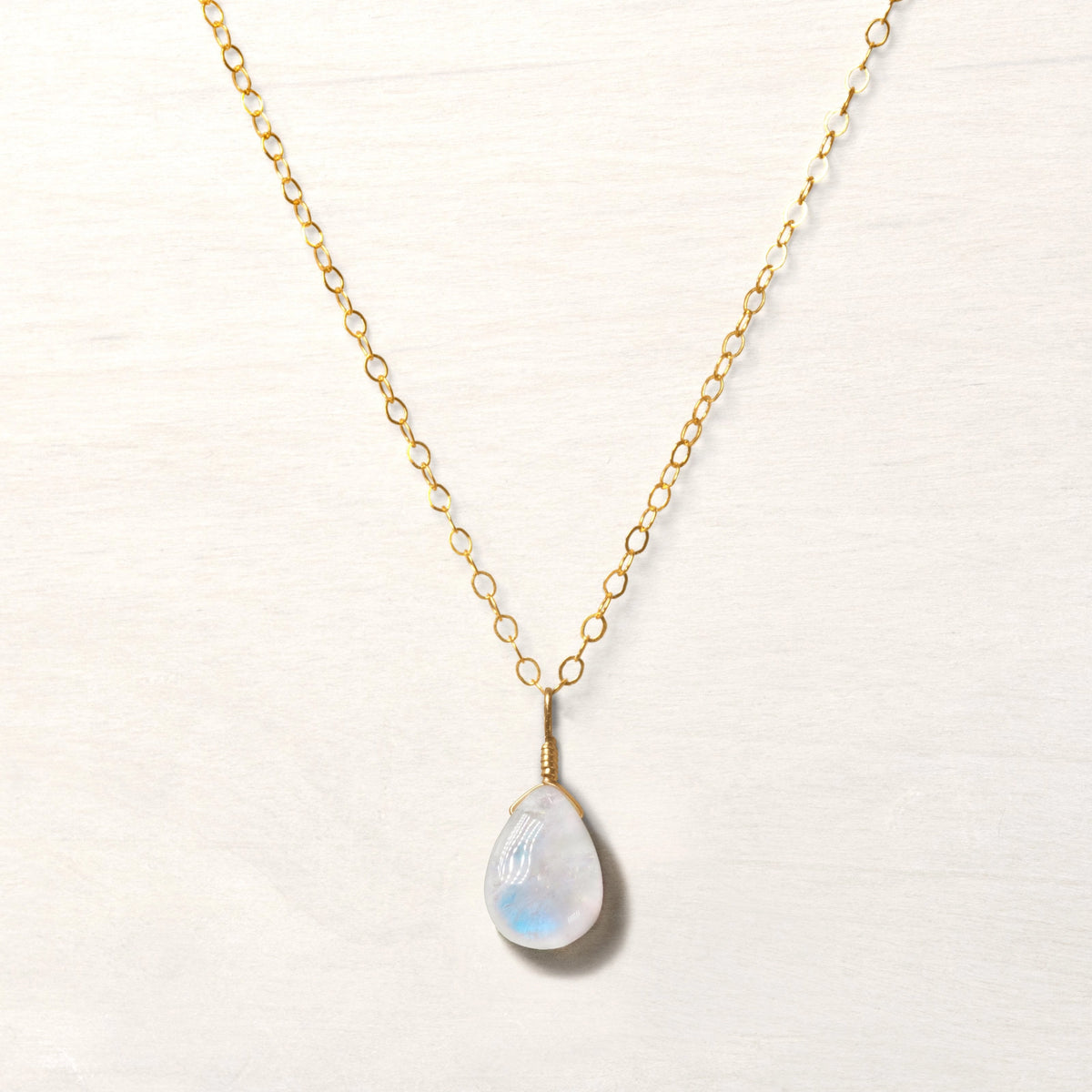 A moonstone teardrop shaped necklace on a gold chain.