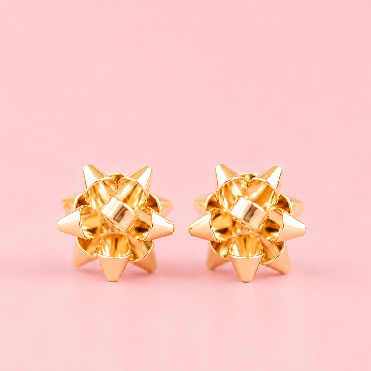 On a pink background is a pair of silver earrings in the shape of holiday bows.