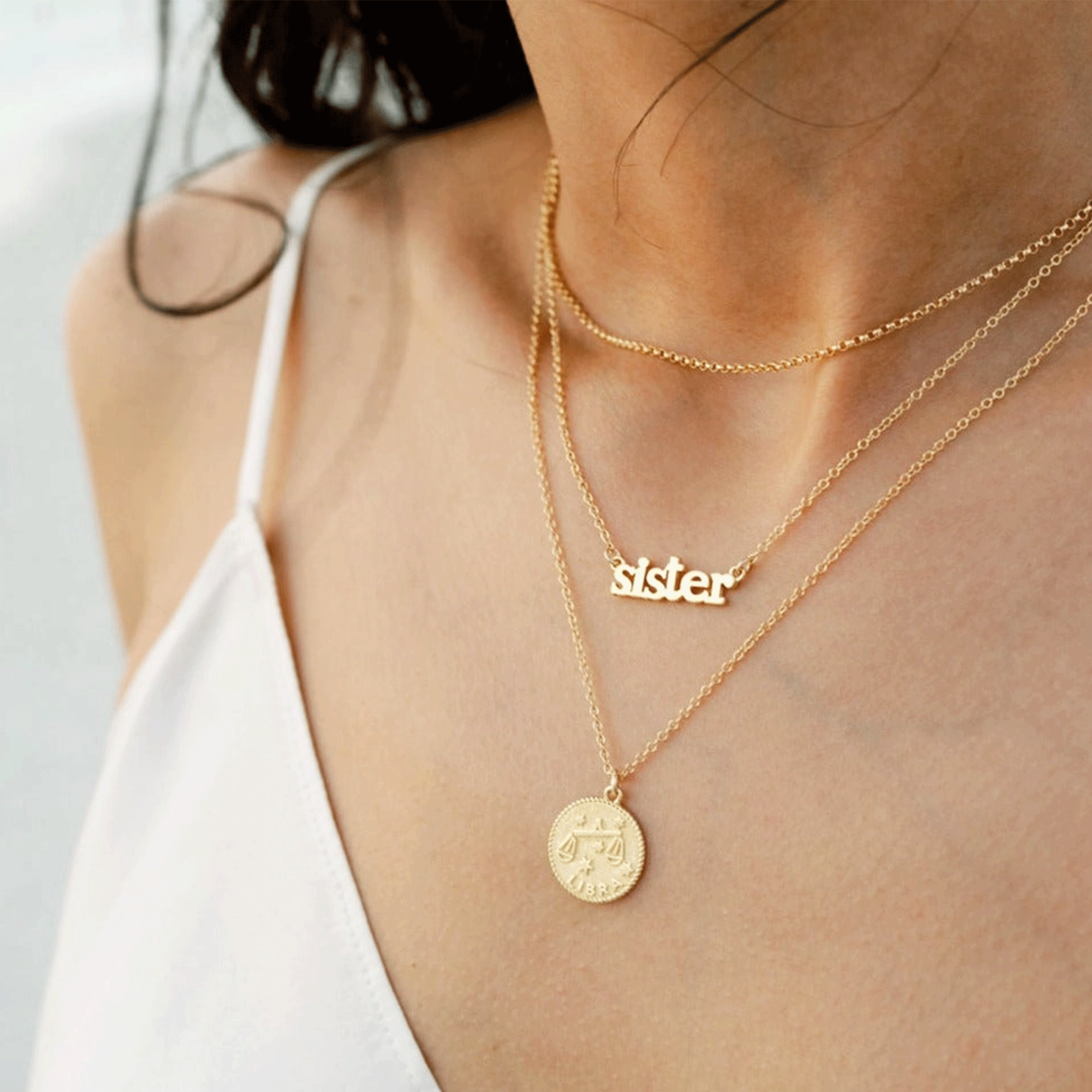 A model wearing the dainty gold chain necklace with a gold plated charm that reads, &quot;sister&quot;. 