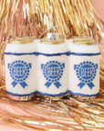 On a pink background with gold tinsel is a glass ornament in the shape of a six pack of beer with a blue label on the front and silver glitter detailing.