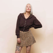 Person wearing a brown blouse and leopard print skirt against a plain background