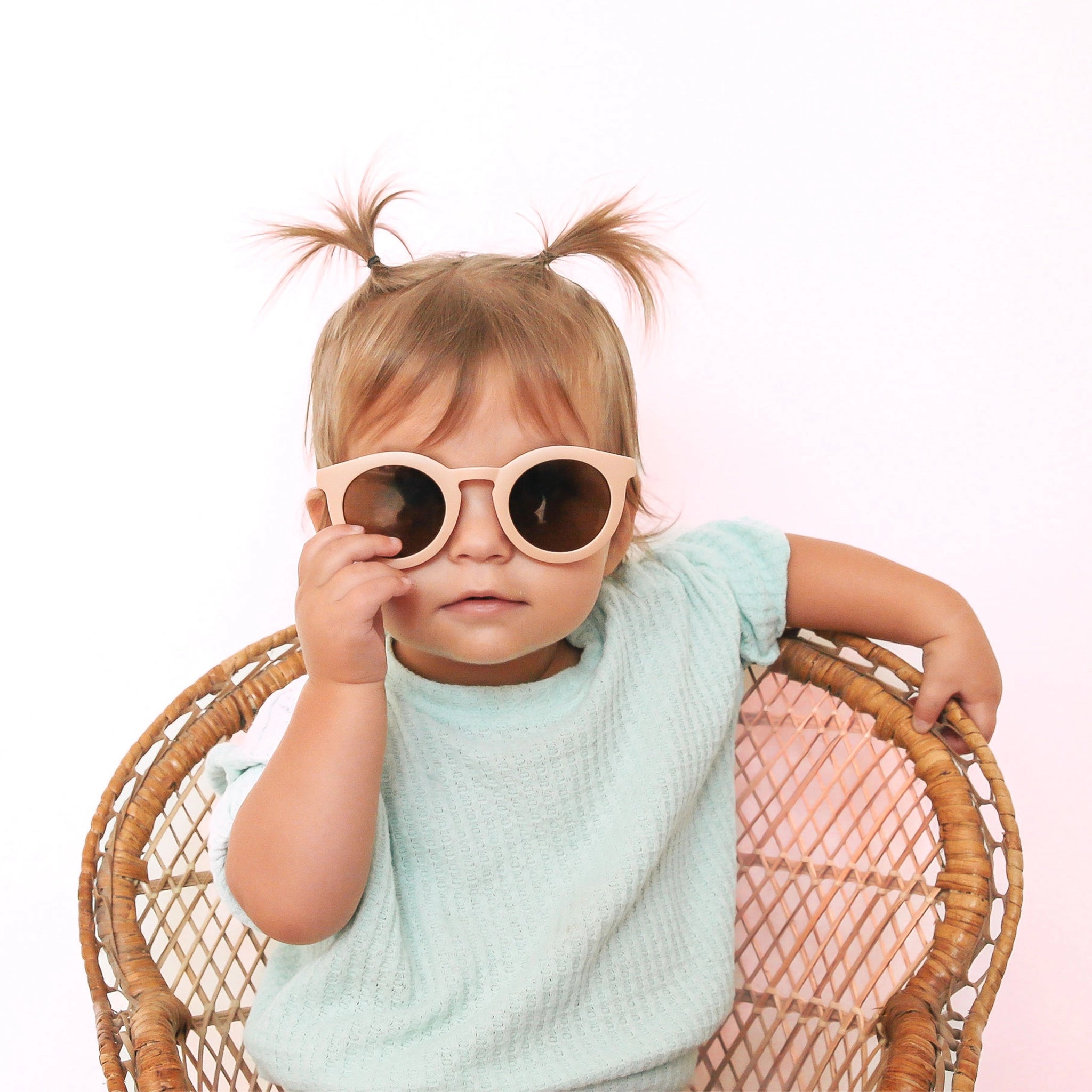 On a white background is a children&#39;s model wearing a pair of light pink round shaped sunglasses. 