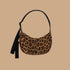 A leopard print curved crescent shaped handbag with a black strap that can adjust from a shoulder bag length to a crossbody.