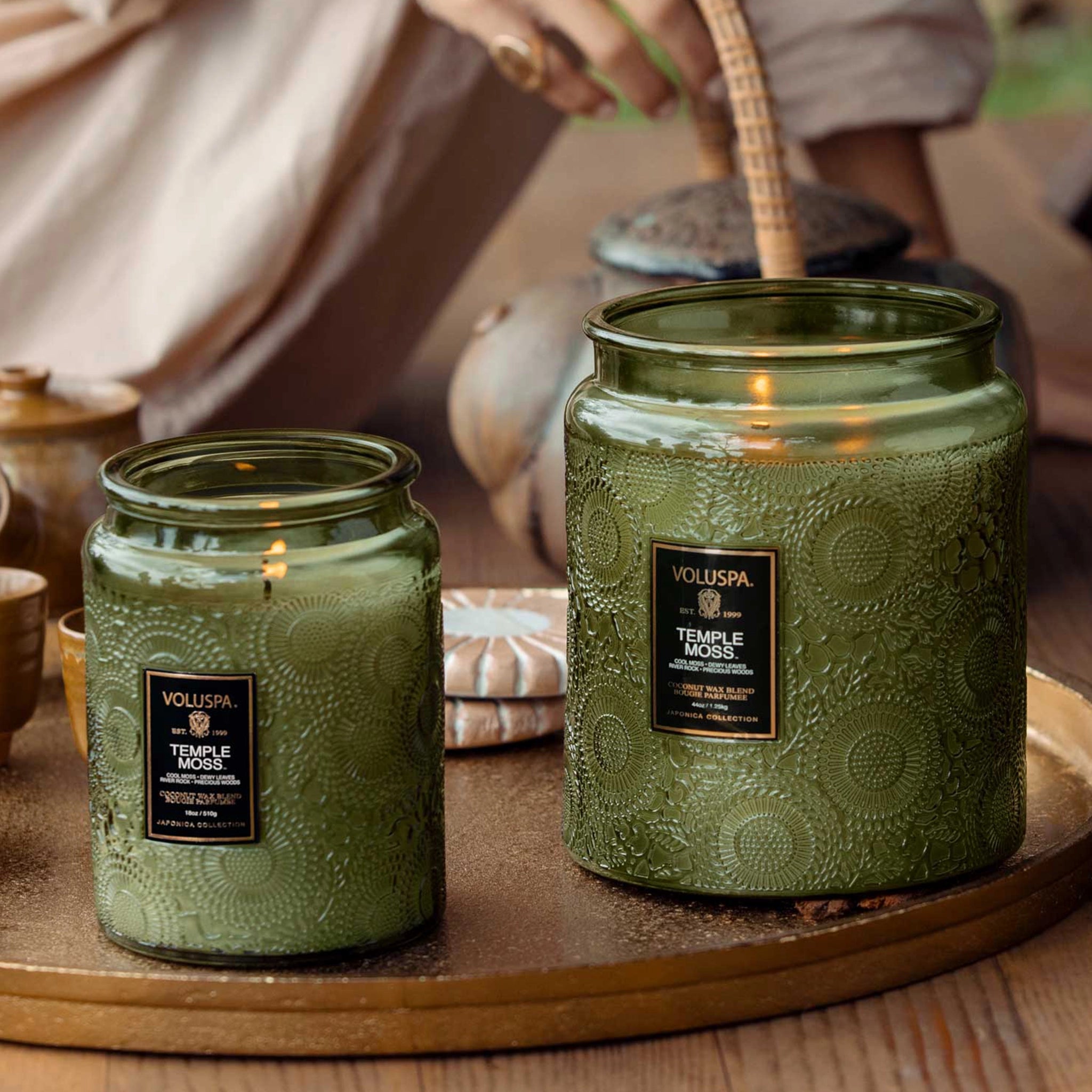 Two decorative green glass jar candles with black labels that read, "Voluspa Temple Moss". The small jar for sale is on the right while the large jar is on the right. 