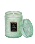 A green glass decorative candle with a single wick and black rectangle label in front that reads, "Voluspa White Cypress".