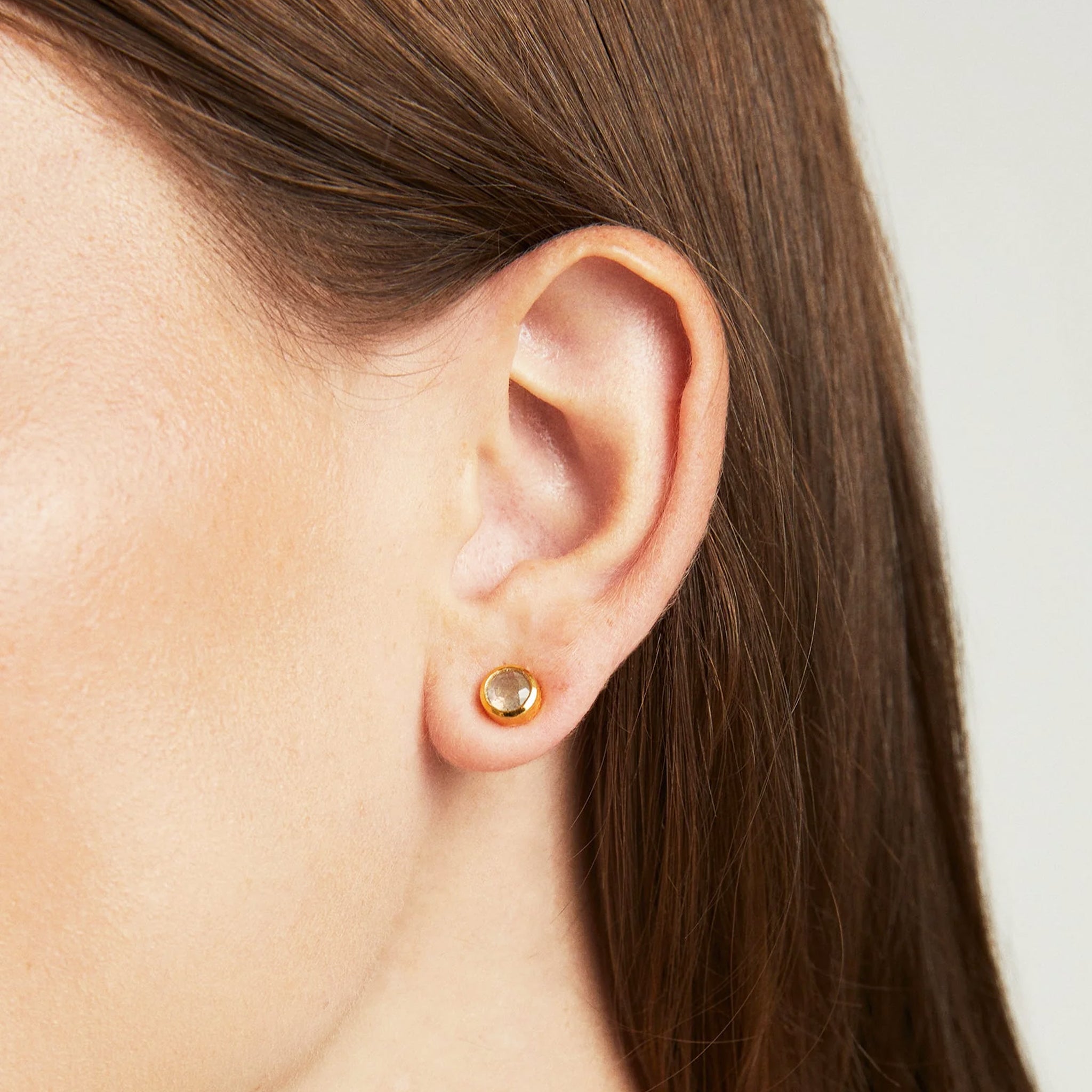 A gold pair of stud earrings with moonstone stone in the center. 