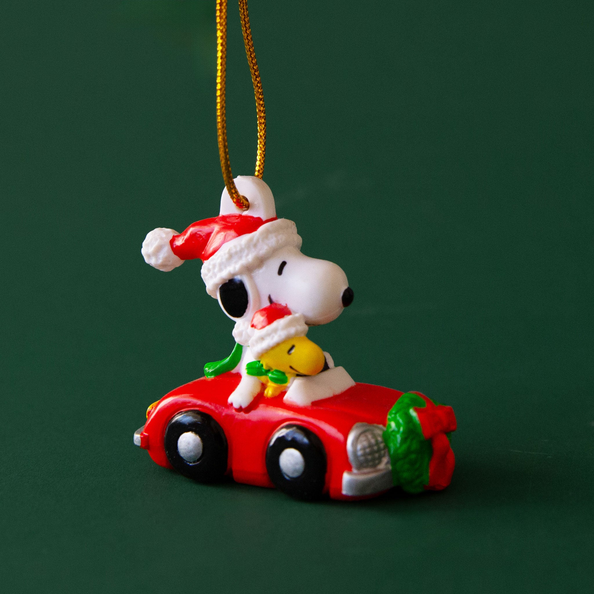 A Snoopy and Woodstock ornament in a vintage red car wearing Santa hats.