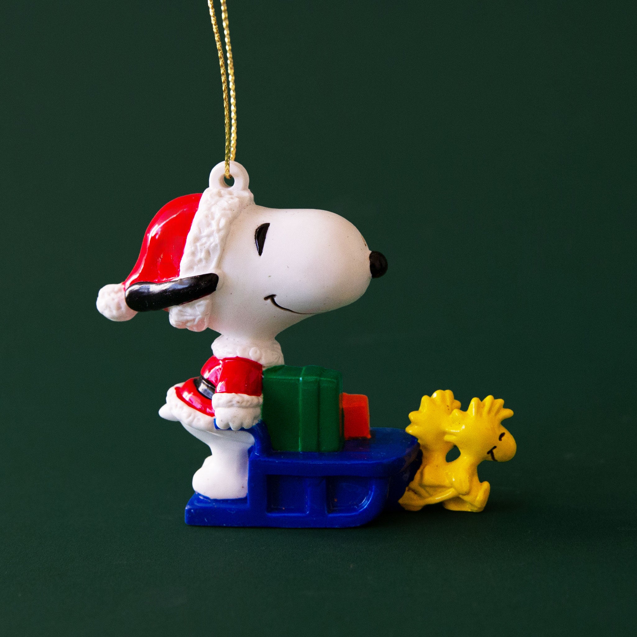 A vintage Snoopy shaped ornament wearing a Santa outfit with a sled. 