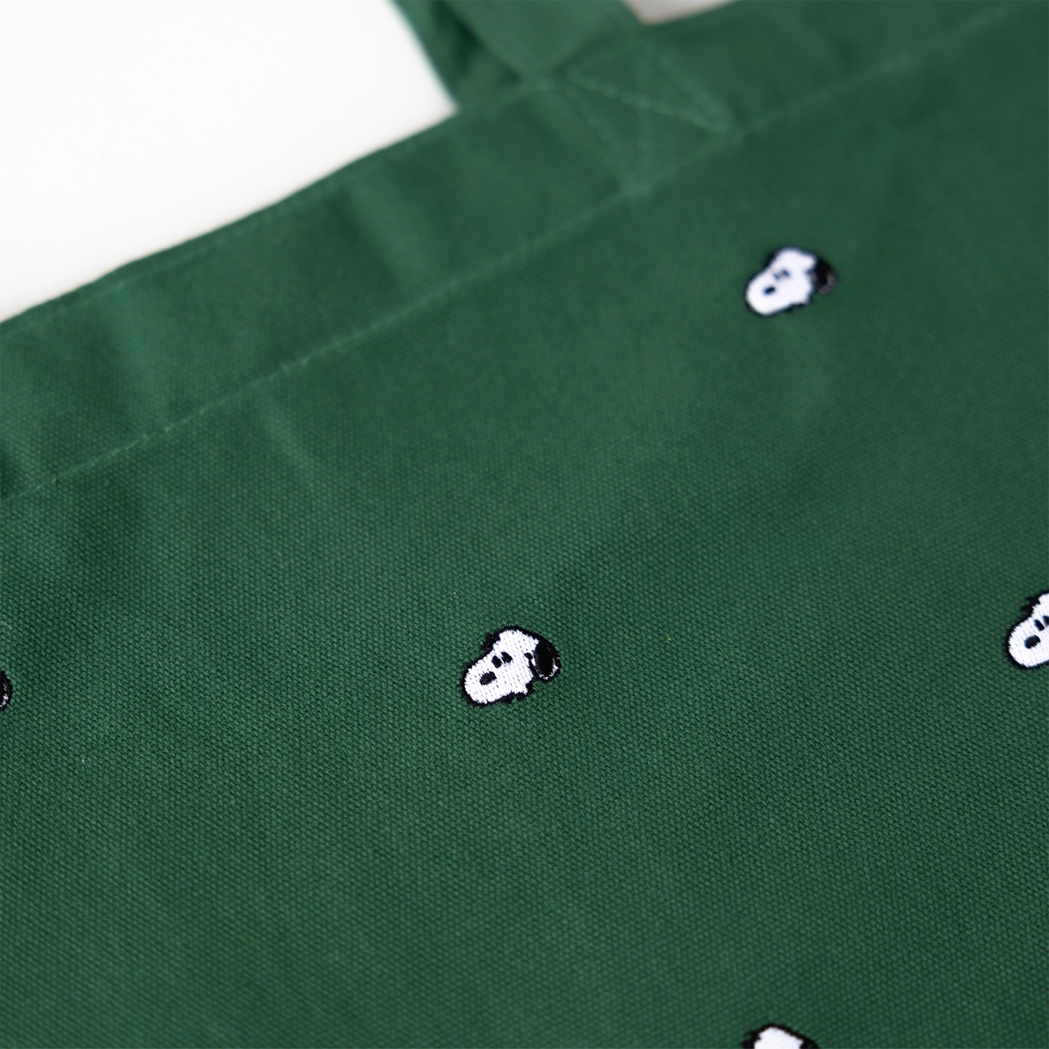 Green fabric with small white and black embroidered snoopy designs on a white background