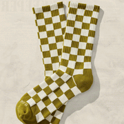 On a cream background is a pair of green and ivory checkered socks. 