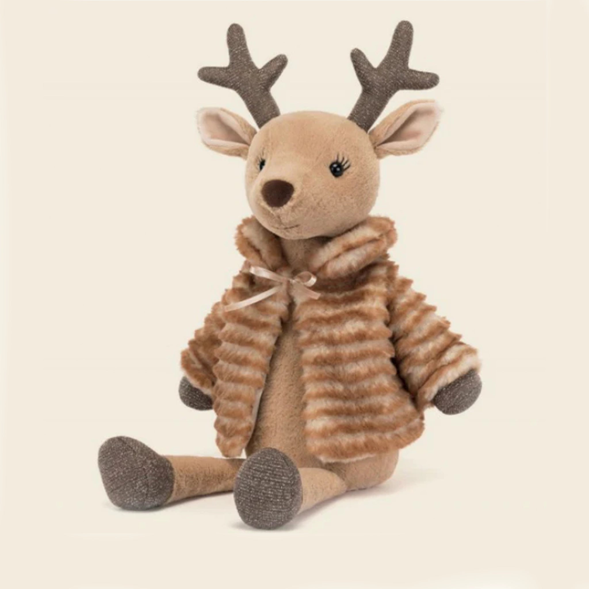 On a cream background is a brown reindeer stuffed animal toy wearing a brown faux fur jacket. 