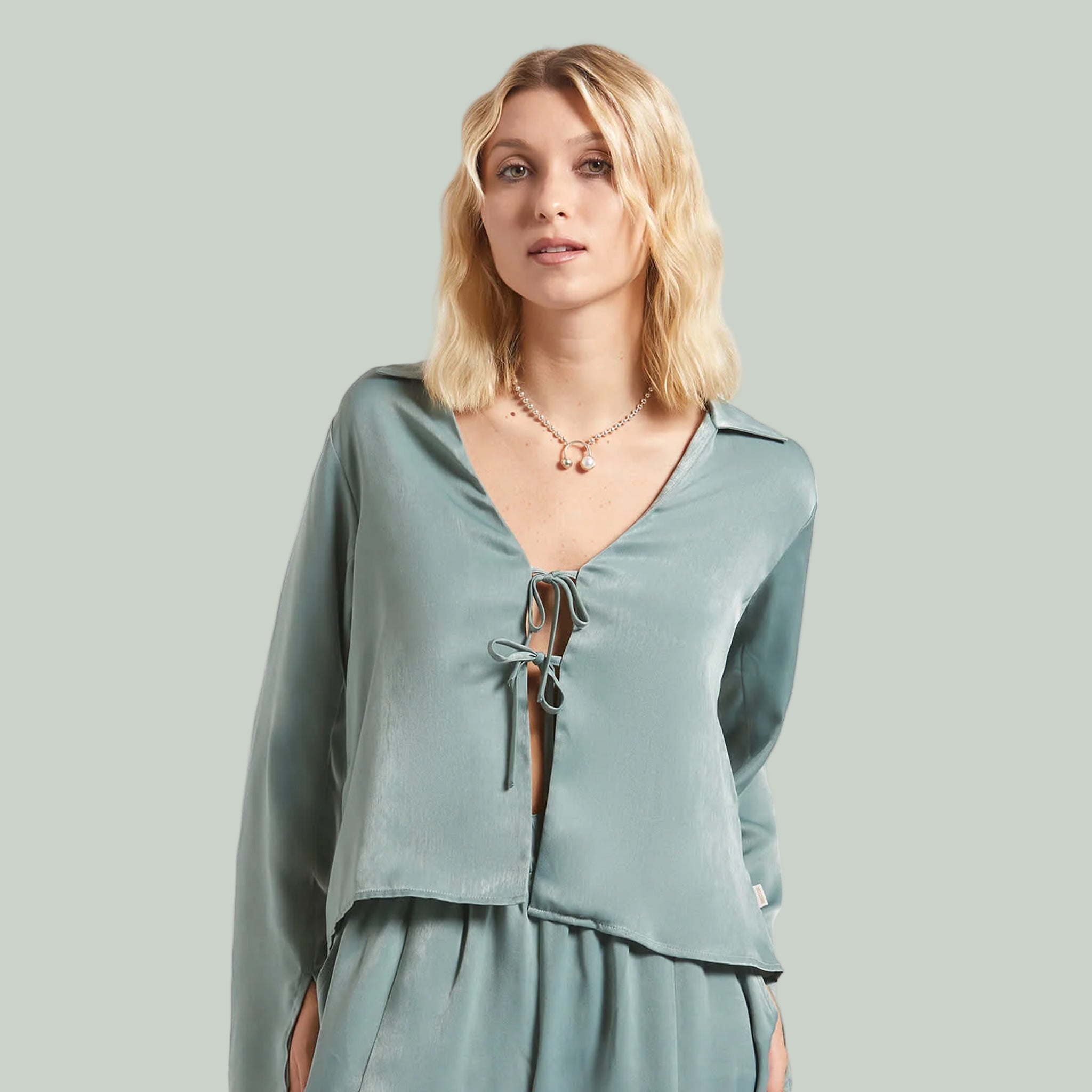 A bluish green silk long sleeve shirt with ties in the center. 