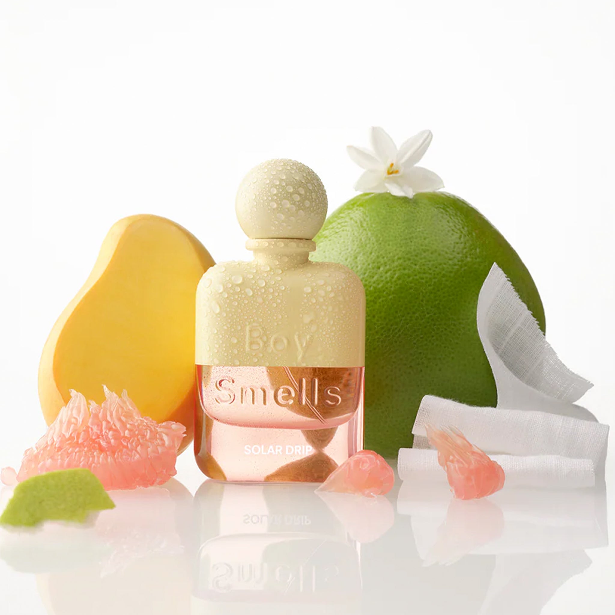 A yellow and pink bottle of perfume next to tropical fruit. 