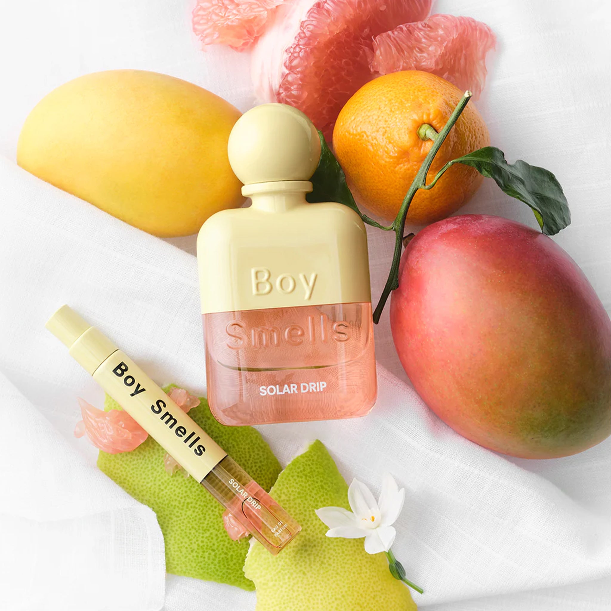 A yellow and pink bottle of perfume next to tropical fruit. 