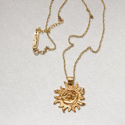 A gold chain necklace with a sun pendant. 