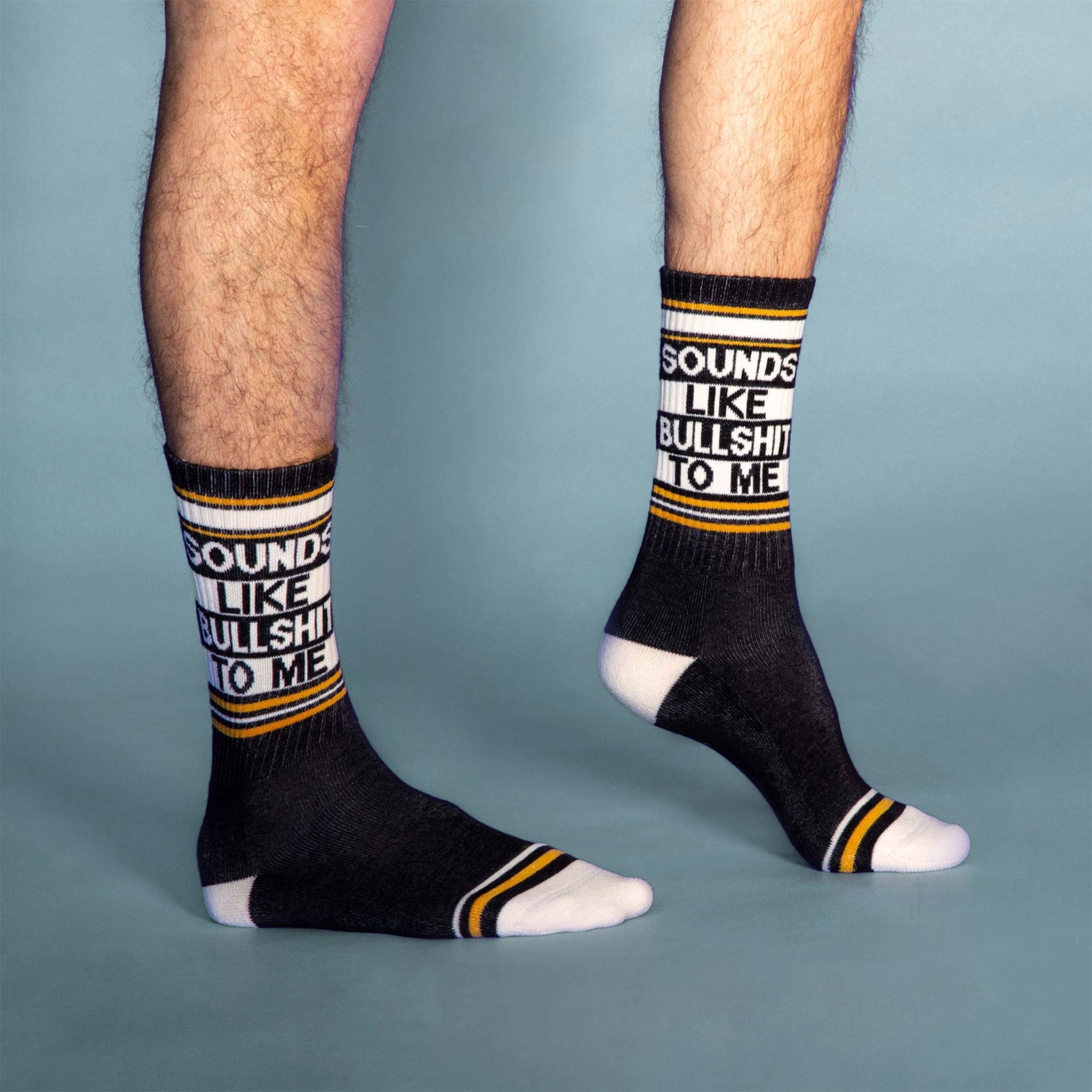 On a blue background is a model wearing a pair of black socks with yellow and white details along with text that reads, &quot;Sounds Like Bullshit To Me&quot;.