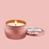 A rosy pink round candle sits in the middle of frame with the lid off to the right.  The tin is a metallic pink color and the candle flame is lit on open candle side.  The lid sits to the right of the candle and reads "Voluspa Sparkling Rose".
