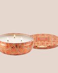 A round orange tin candle with three wicks and text on the lid that reads, 'Voluspa Spiced Pumpkin Latte'. 