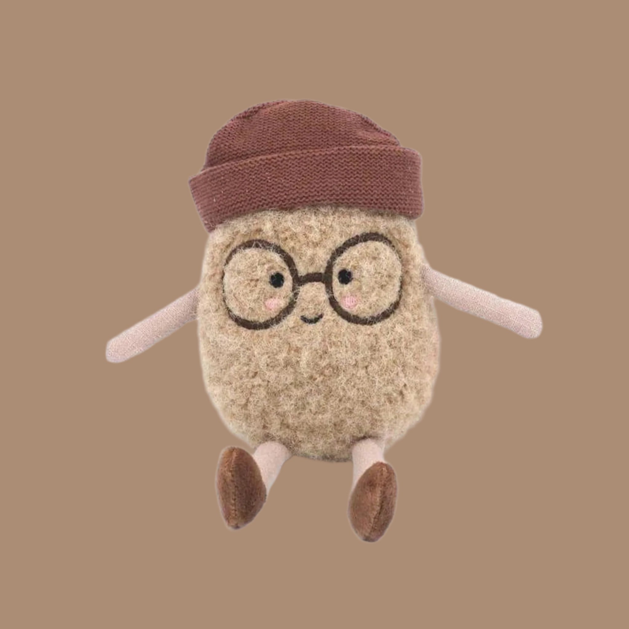 A spud potato shaped stuffed toy with a smiling face, round embroidered glasses and a brown beanie and shoes. 