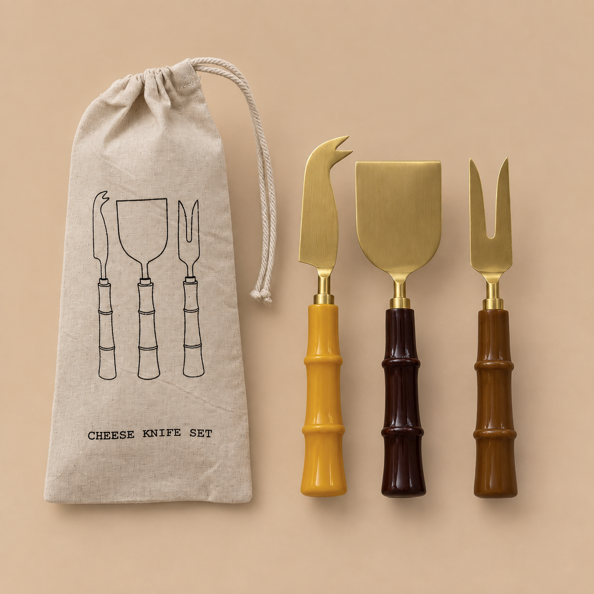 A cheese knife set with three utensils and a drawstring pouch on a warm beige background. The utensils have gold-toned metal heads with handles in mustard yellow, dark brown, and medium brown bamboo-style finishes.