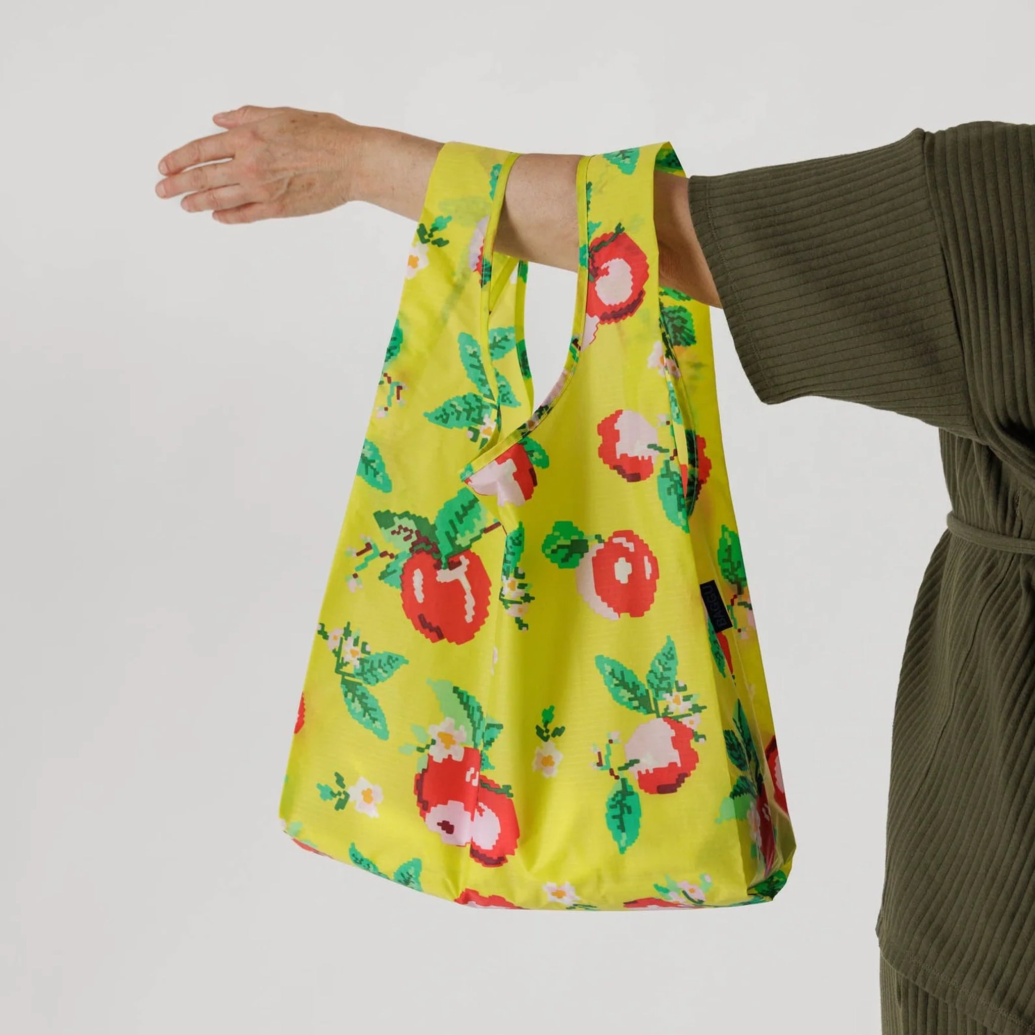 On a grey background is a neon green nylon bag with a red apple pattern. 