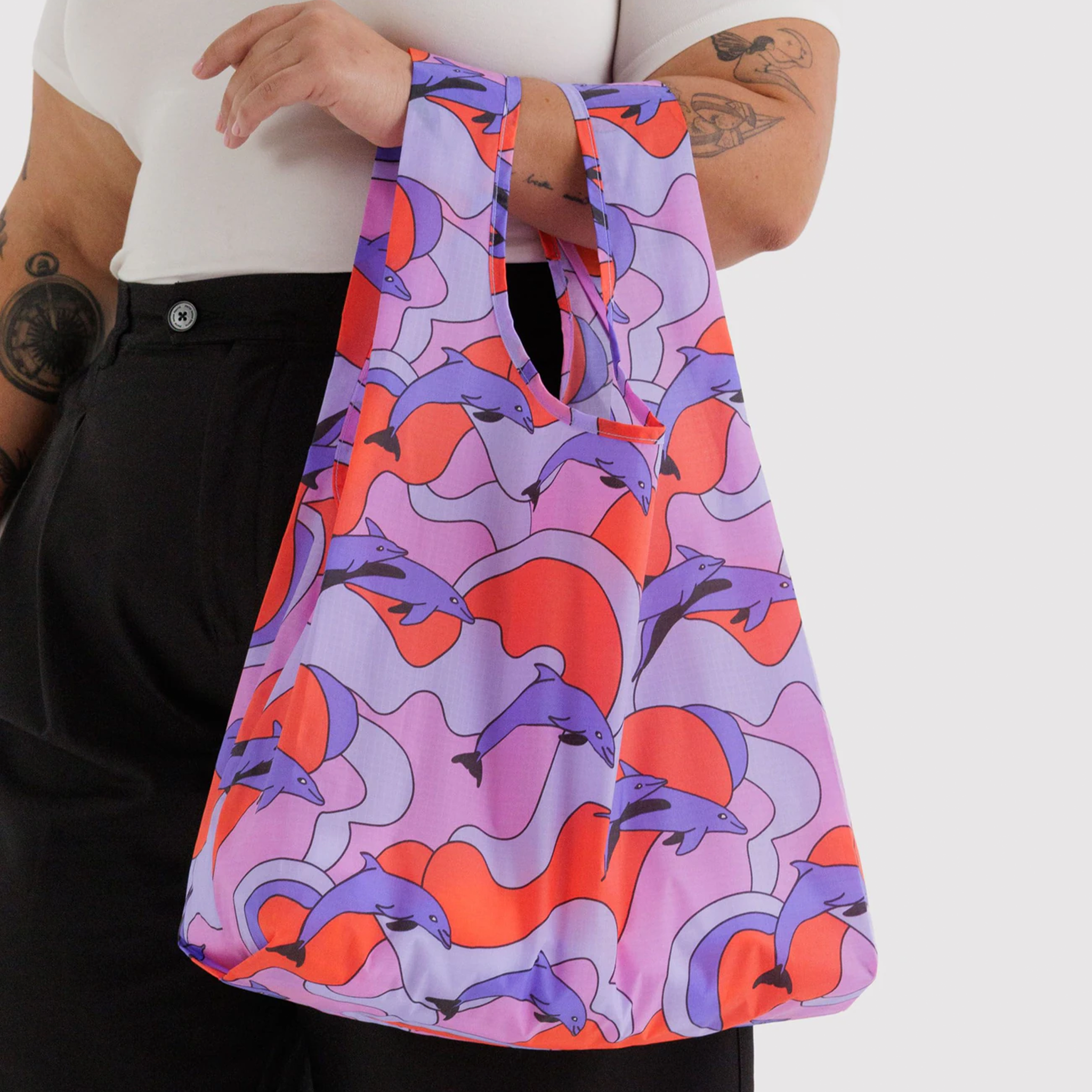 A reusable bag with red, pink and purple dolphins and details on a model's arm.