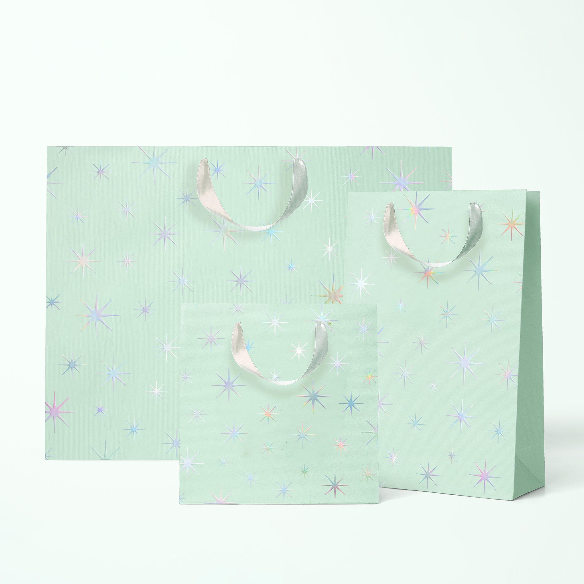 Three different sized mint colored gift bags with silver holographic star patterns and silver ribbon handles. 