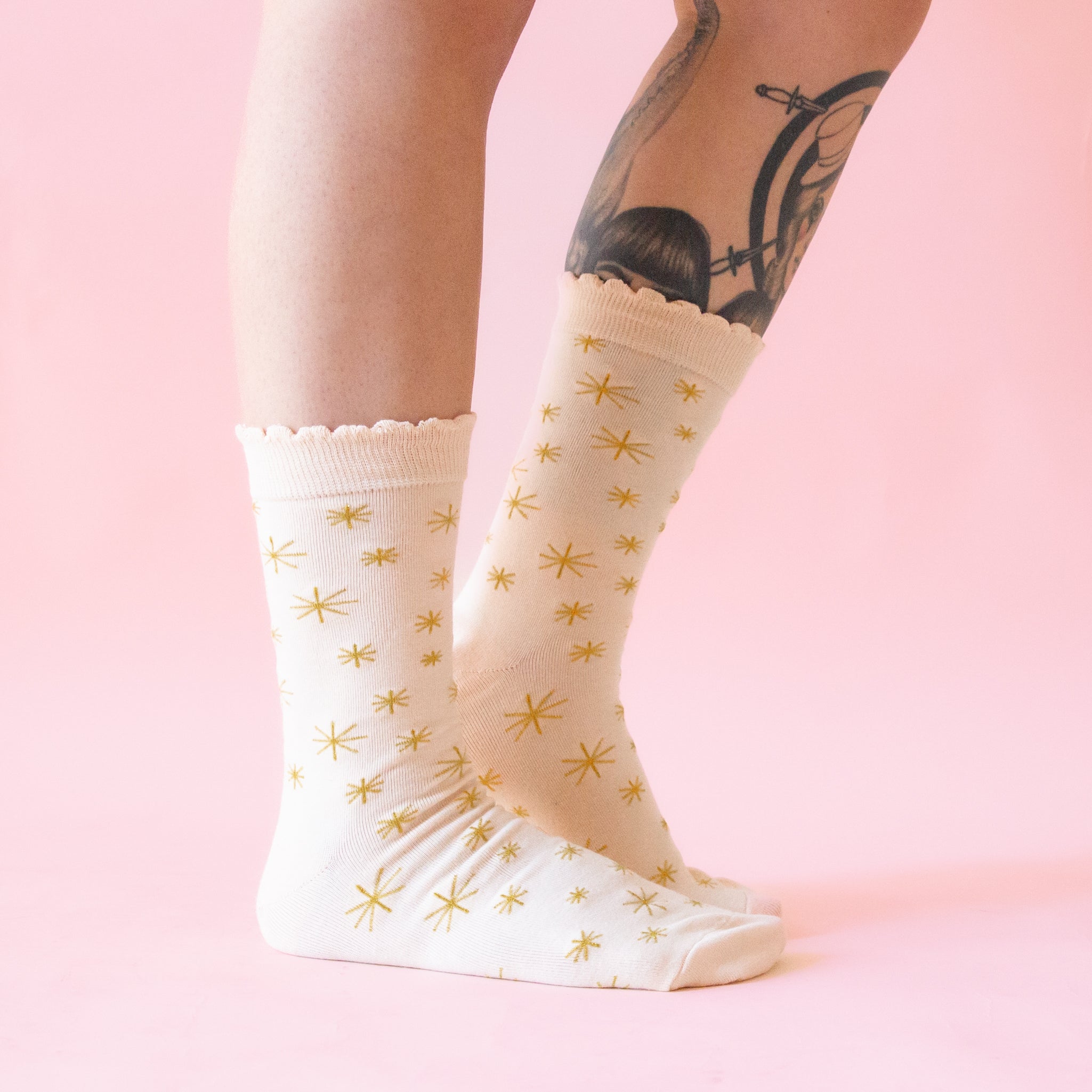 A pair of cream colored socks with a gold star pattern. 