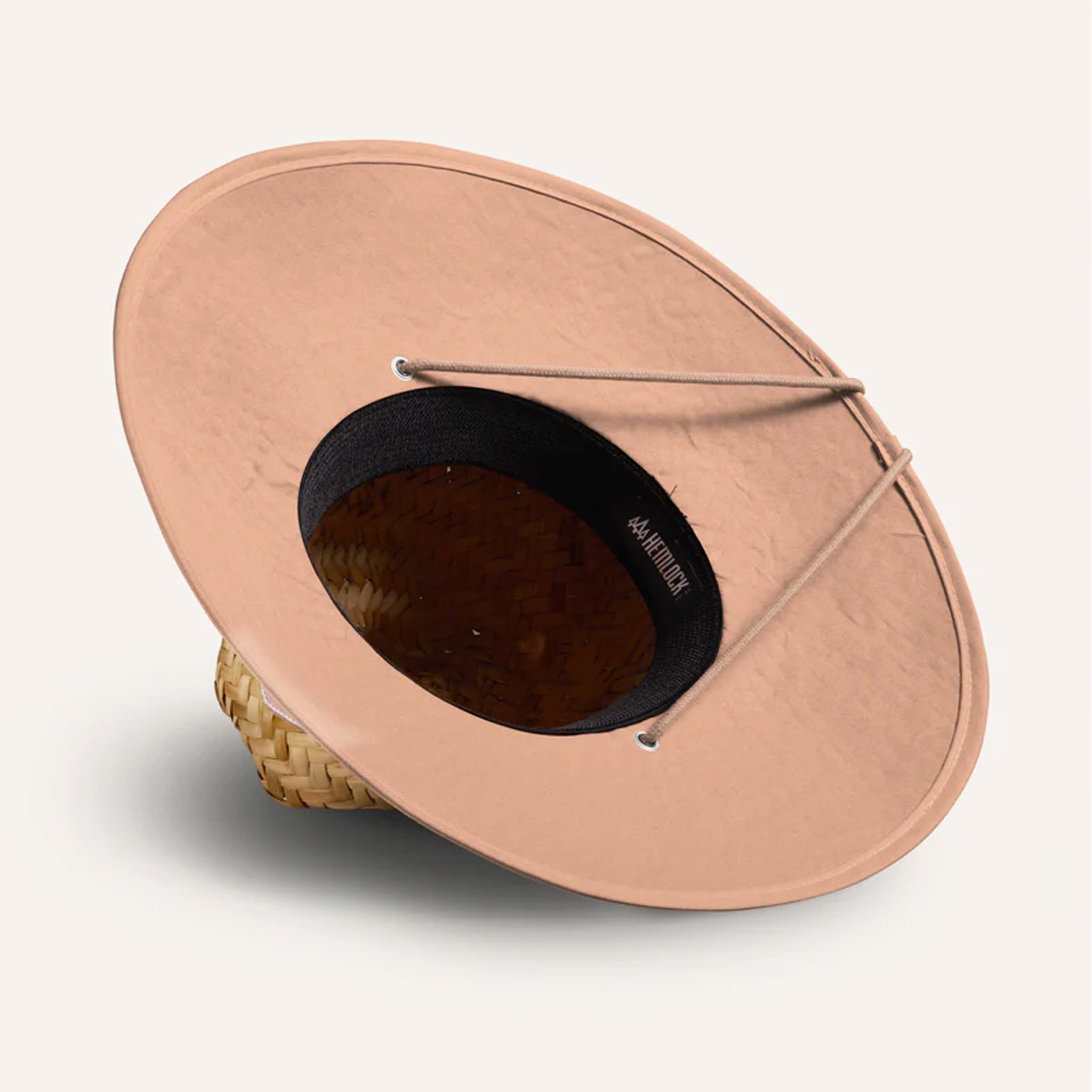 On a white background is a straw hat with a neutral mauve / tan brim underneath and neck strap. 