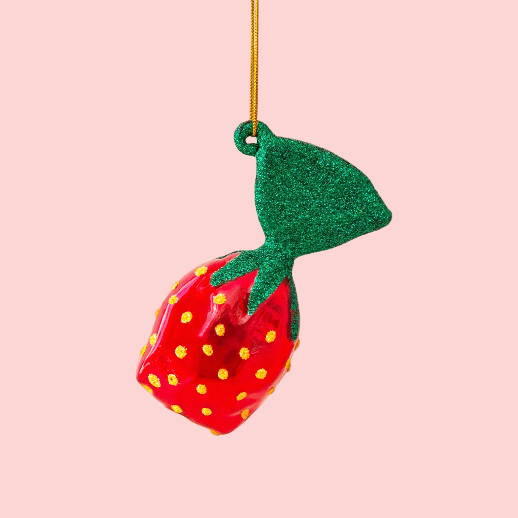 A strawberry hard candy shaped Christmas ornament on a pink background.