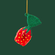 A strawberry hard candy shaped Christmas ornament on a pink background.