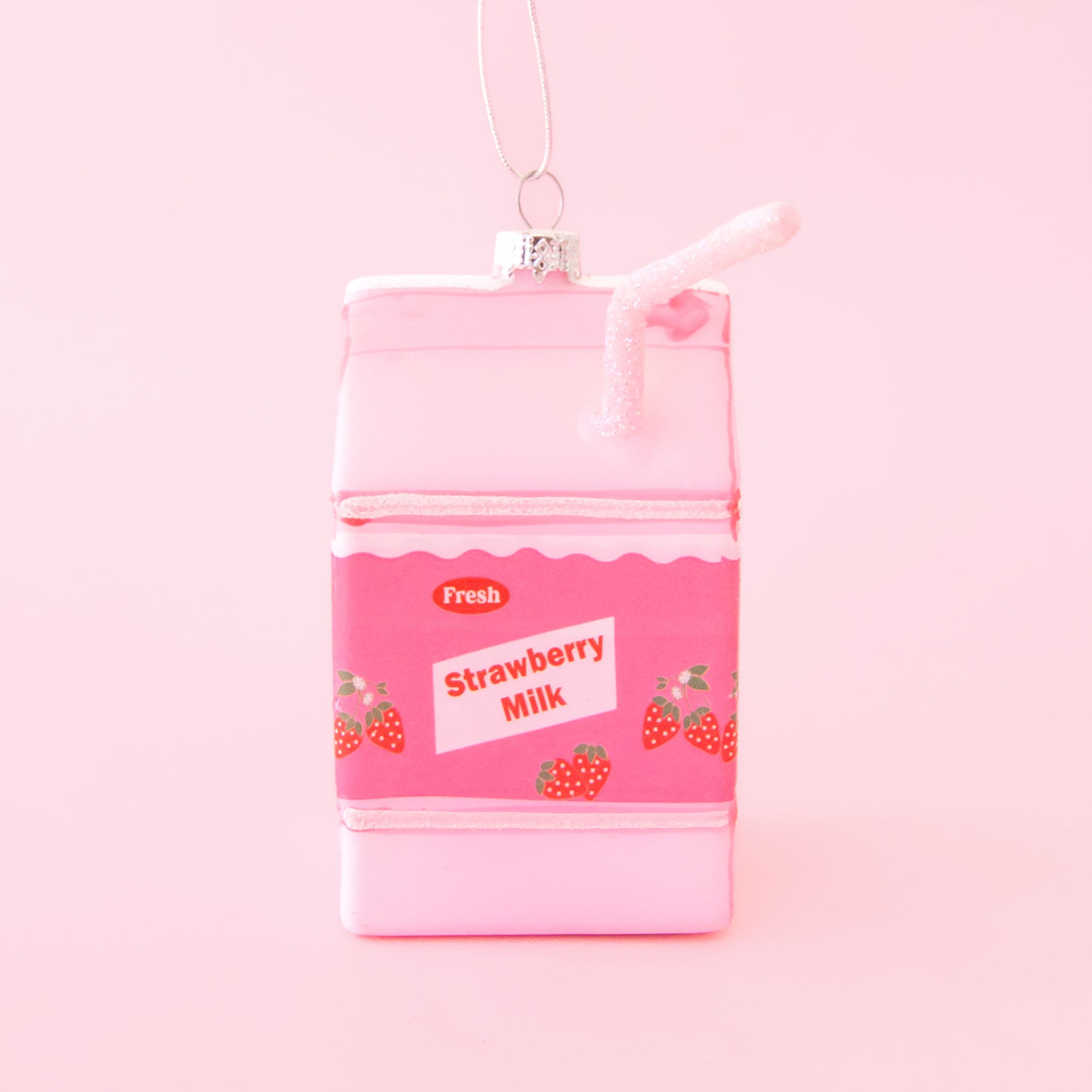 A pink glass strawberry milk carton shaped ornament with text that reads, &#39;Fresh Strawberry Milk&#39;. 